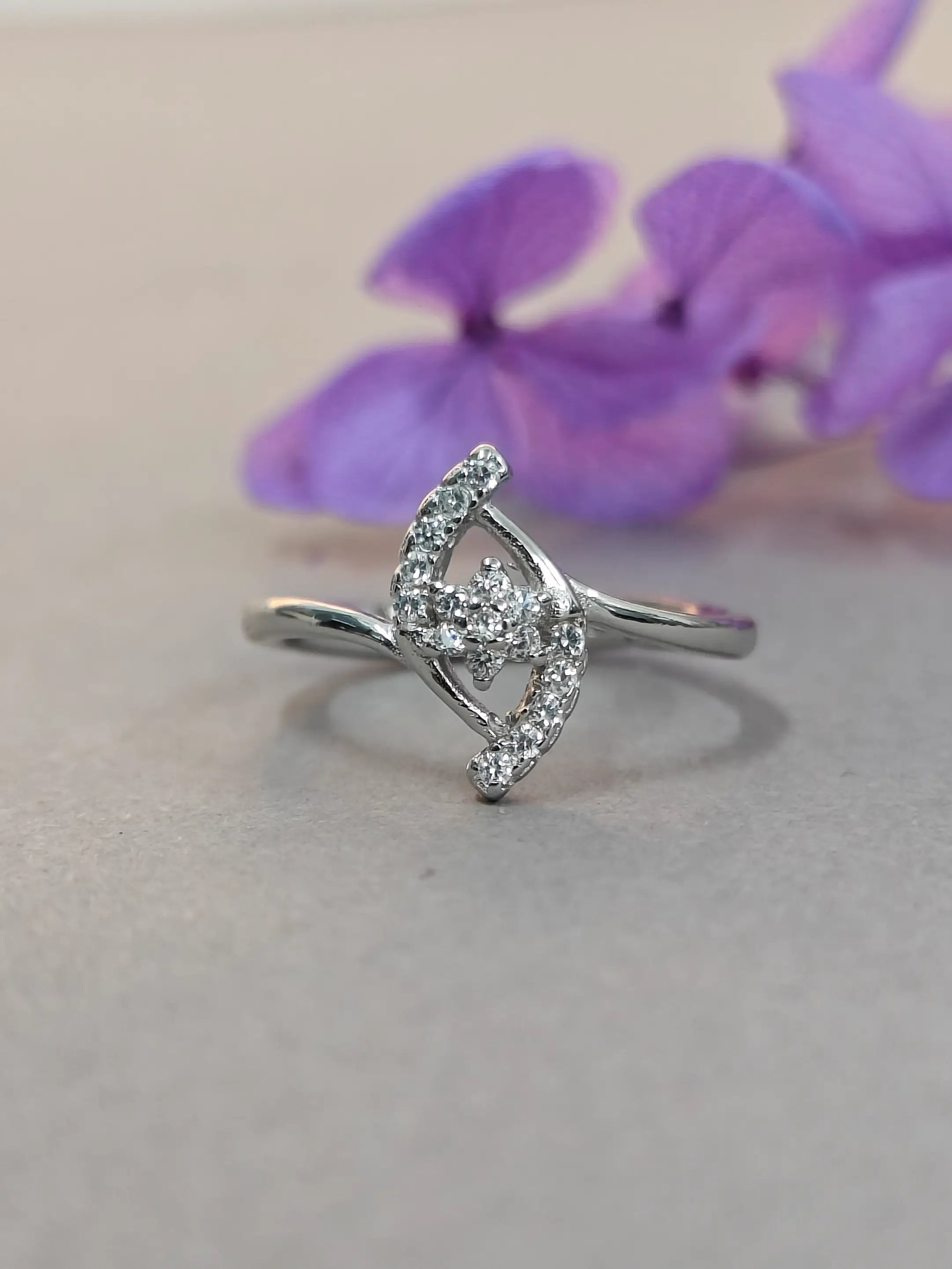 Silver ring with gemstones on a light gray background with purple flowers.